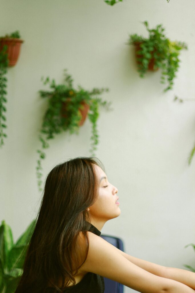 A peaceful side profile of a woman meditating with green plants in the background.
